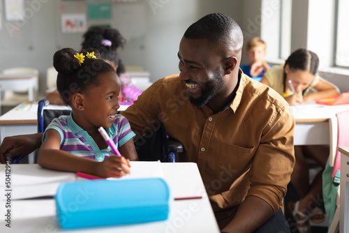 Smiling african american young male teacher looking at african american elementary schoolgirl