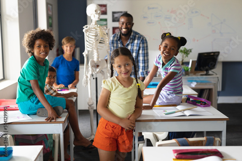 Portrait of multiracial students and african american young male teacher with skeleton in class