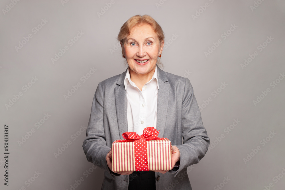 Happy surprised woman senior lady posing with gift box on grey background Happy surprised woman senior lady posing with gift box on grey background