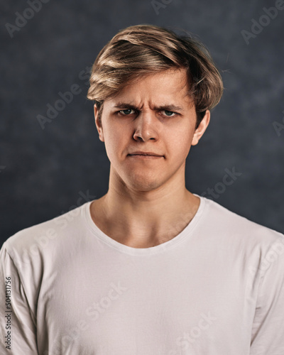young man frowning on gray background. Human emotions photo