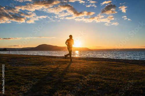 Silhouette image of a man running by Lake Rotorua at sunset, Rotorua, New Zealand.