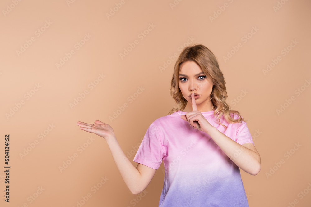 pretty woman showing hush sign and pointing with hand isolated on beige.