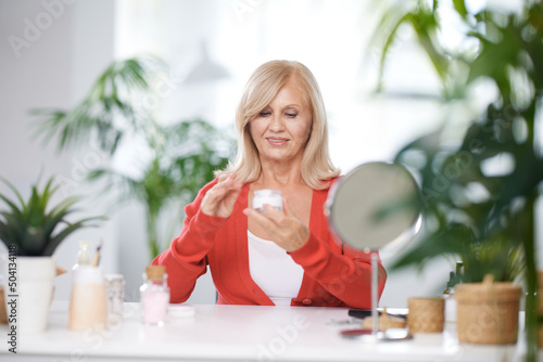 A senior woman opening anti age creme while sitting at home in front of mirror.