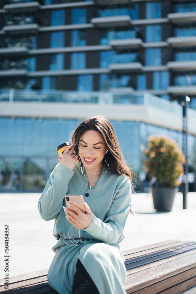 Fototapeta premium Beautiful business woman enjoying coffee break on free time outdoor with favorite music in earphones, millenial female listening audio book on mobile app