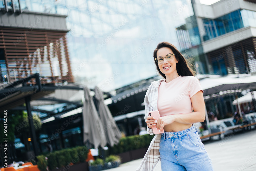 Fototapeta premium Pretty young hipster female posing on street with smartphone, cute hipster fashionable woman with sexy body strolling outdoors
