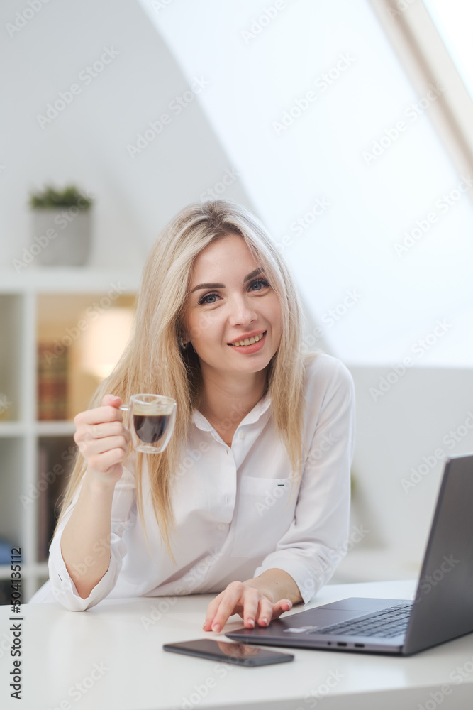 Young beautiful caucasian blonde woman working on laptop at home and drinking coffee. Remote work or freelance. Young beautiful caucasian blonde woman working on laptop at home and drinking coffee. Remote work or freelance.