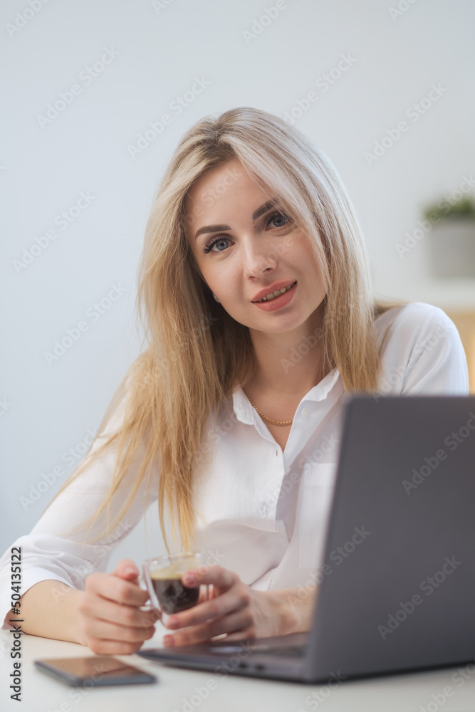 Young beautiful caucasian blonde woman working on laptop at home and drinking coffee. Remote work or freelance. Young beautiful caucasian blonde woman working on laptop at home and drinking coffee. Remote work or freelance.