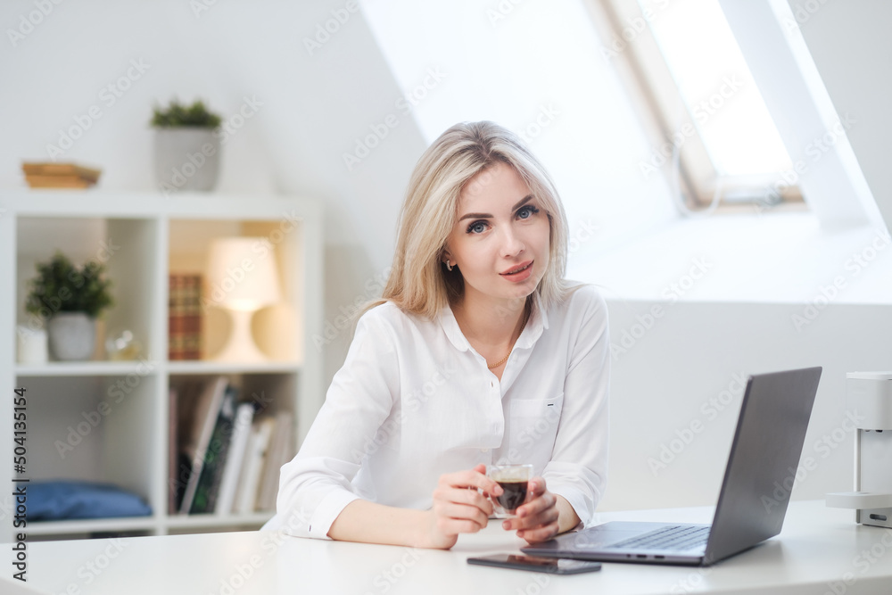 Young beautiful caucasian blonde woman working on laptop at home and drinking coffee. Remote work or freelance. Young beautiful caucasian blonde woman working on laptop at home and drinking coffee. Remote work or freelance.