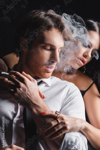 Sexy woman hugging boyfriend with cigarette on black background.