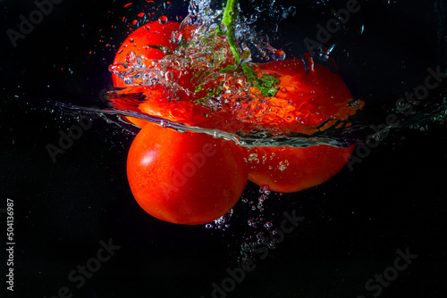 Fresh red tomato falling into water with water splash and air bubbles isolated on black background