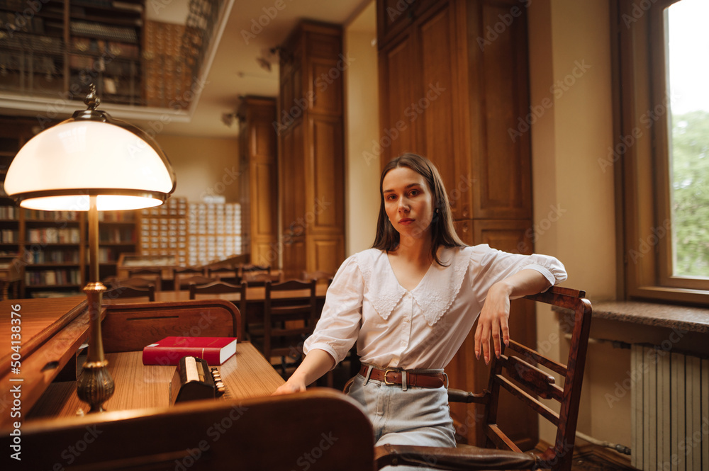 Portrait of an attractive woman in a white blouse sitting at a public library at a table and posing for the camera. Portrait of an attractive woman in a white blouse sitting at a public library at a table and posing for the camera.