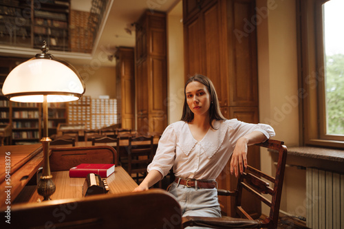 Portrait of an attractive woman in a white blouse sitting at a public library at a table and posing for the camera.