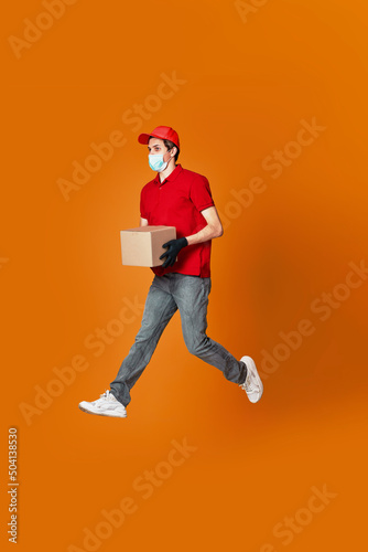 Delivery man in face mask holding cardboard box and jumping