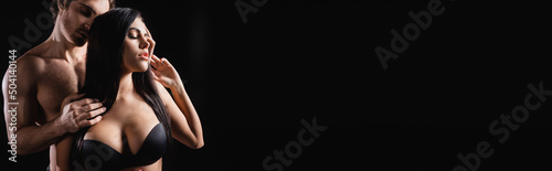 Shirtless man touching hair of sensual girlfriend in bra isolated on black, banner.
