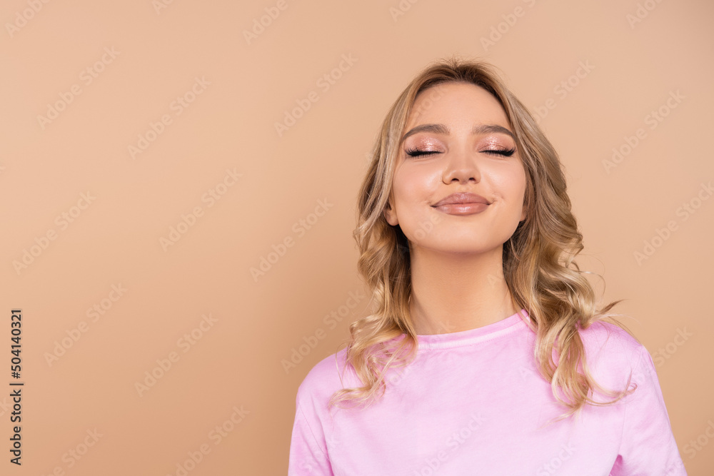 pleased young woman smiling with closed eyes isolated on beige. pleased young woman smiling with closed eyes isolated on beige.