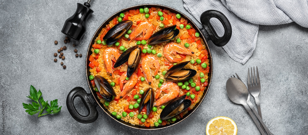 Traditional Spanish paella with seafood in a frying pan. Gray concrete grunge background. Top view, flat lay. Mediterranean food. Paella with prawns and mussels. Banner