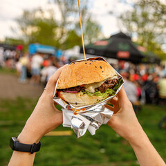 Big burger in hands at street food outdoor festival