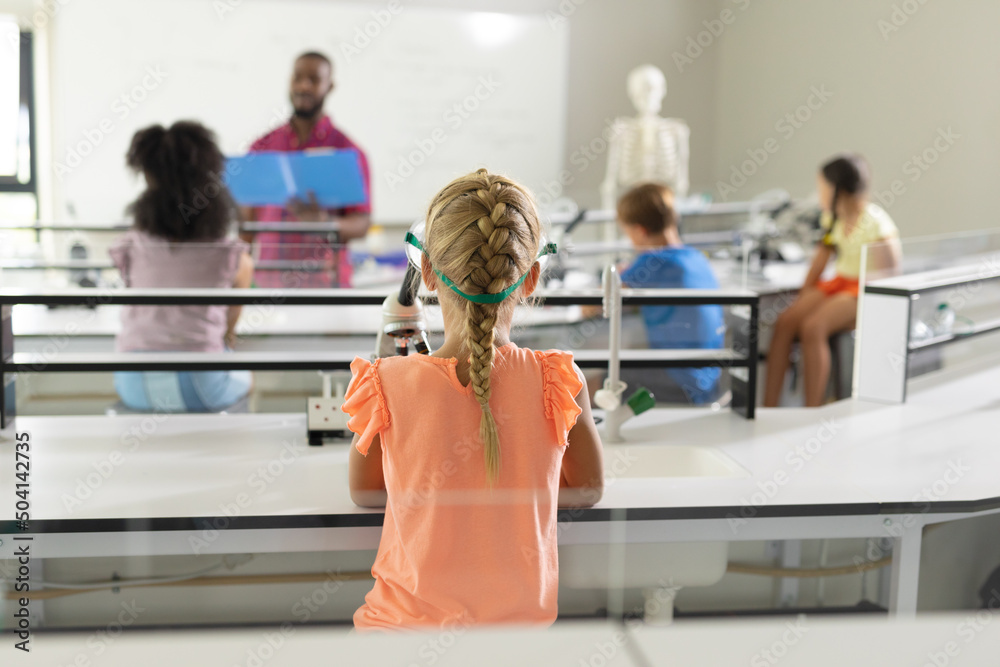 Obraz premium Rear view of multiracial elementary students listening to african american young male teacher in lab
