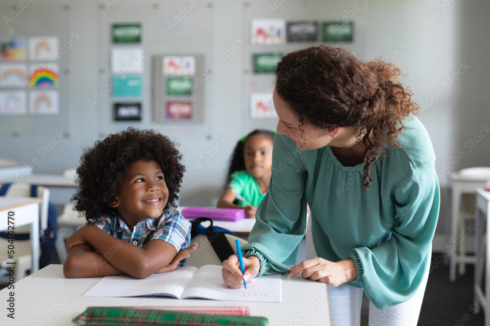 Caucasian young female teacher teaching african american elementary schoolboy studying at desk Caucasian young female teacher teaching african american elementary schoolboy studying at desk