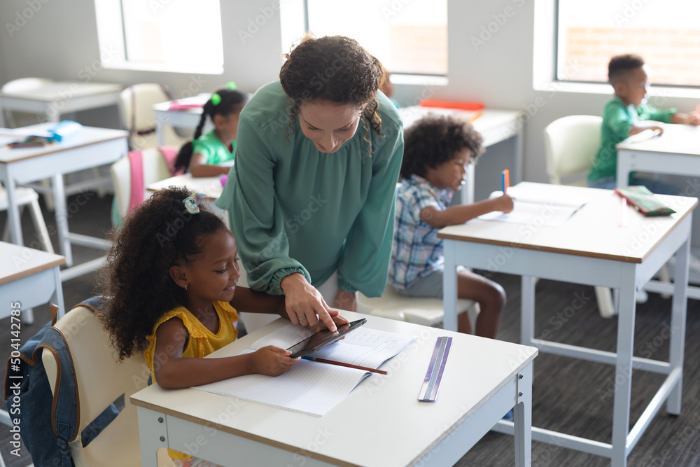 Young caucasian female teacher showing digital tablet to african american elementary schoolgirl