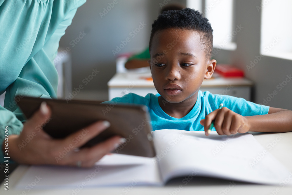 Close-up of caucasian young female teacher showing digital tablet to african american elementary boy Close-up of caucasian young female teacher showing digital tablet to african american elementary boy