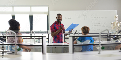 Smiling african american young male teacher gesturing while reading file to multiracial students