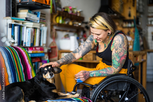 Young woman in wheelchair with her dog at home   © pikselstock