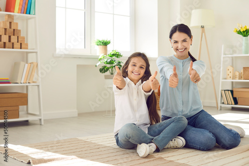 Portrait of overjoyed young Caucasian mother and small teen daughter show thumb up recommend learning studying course online. Smiling mom and little girl child give recommendation to service. photo