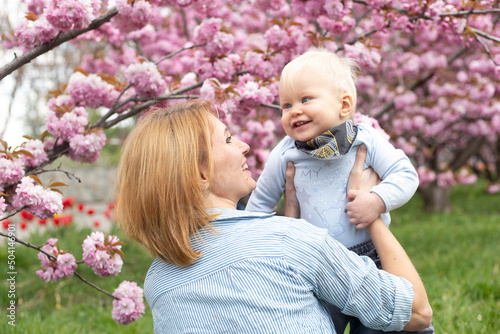 happy hipster woman with little baby boy near pink sakura blooming tree. Spring concept