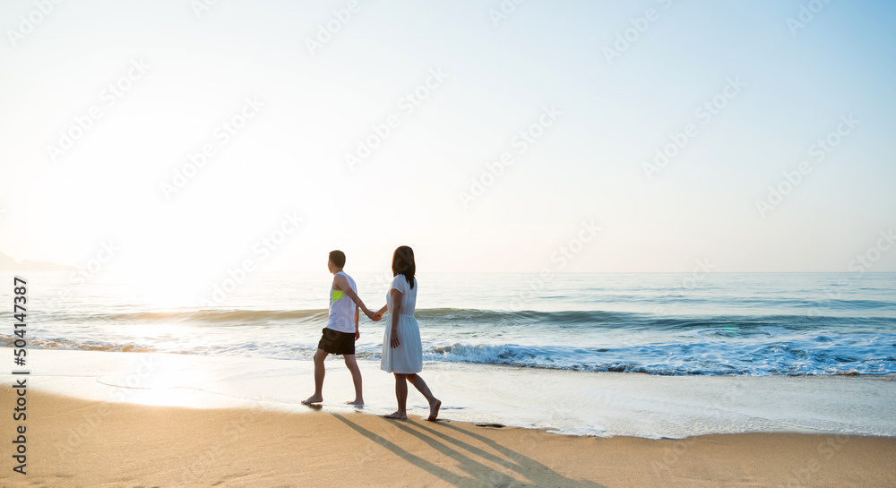 Young couple holding hand walking on beach.