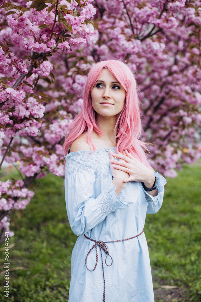 happy woman near pink sakura blooming tree in blue dress