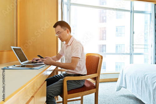 Man using laptop and phone in bedroom
