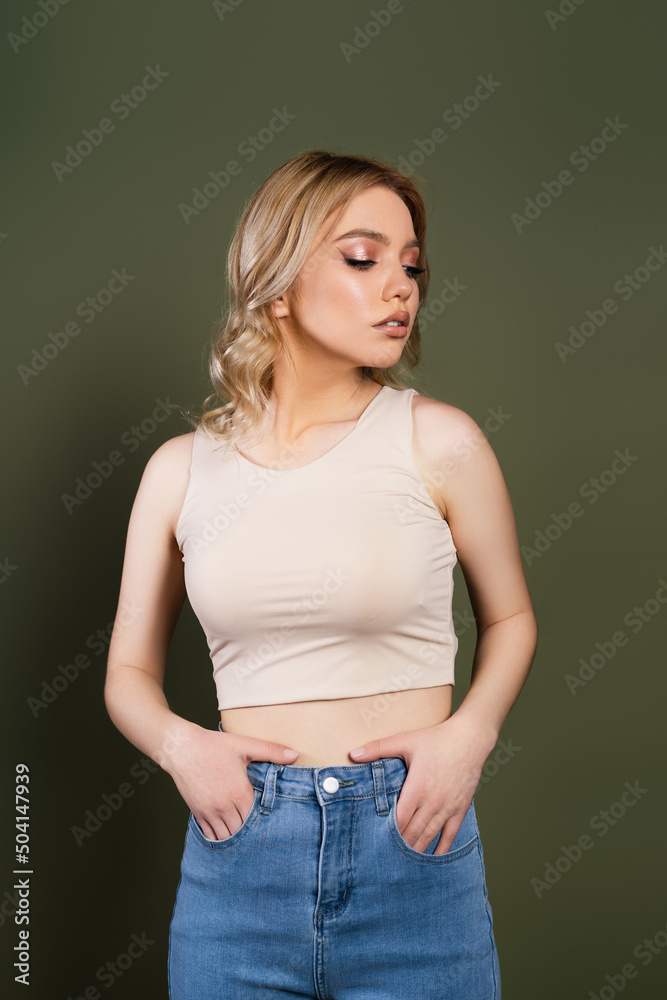 young woman in beige top posing with hands in pockets of jeans isolated on green. young woman in beige top posing with hands in pockets of jeans isolated on green.