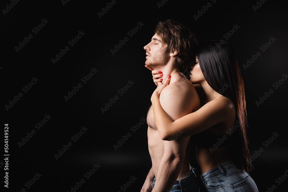 Side view of brunette woman touching neck of muscular boyfriend isolated on black. Side view of brunette woman touching neck of muscular boyfriend isolated on black.