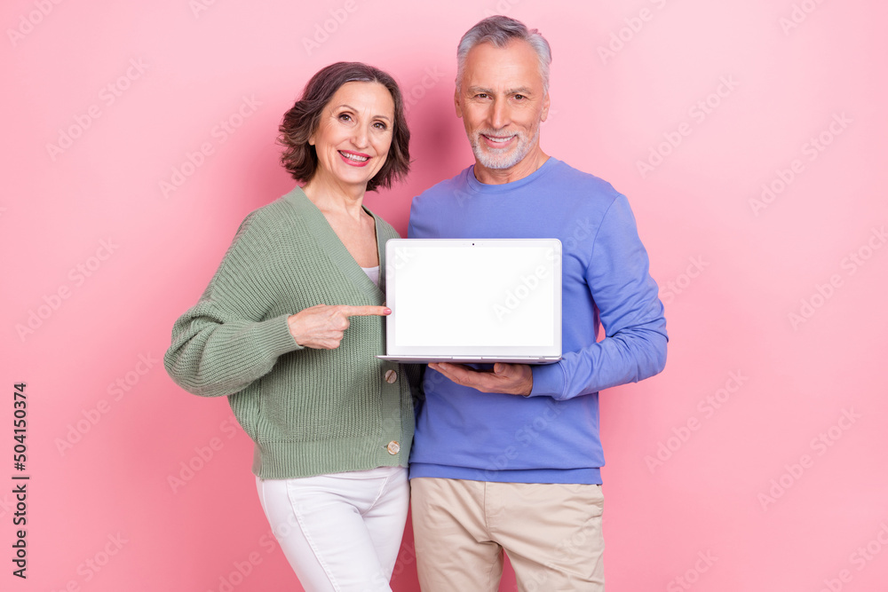 Portrait of two elderly persons direct finger empty space netbook display isolated on pink color background Portrait of two elderly persons direct finger empty space netbook display isolated on pink color background