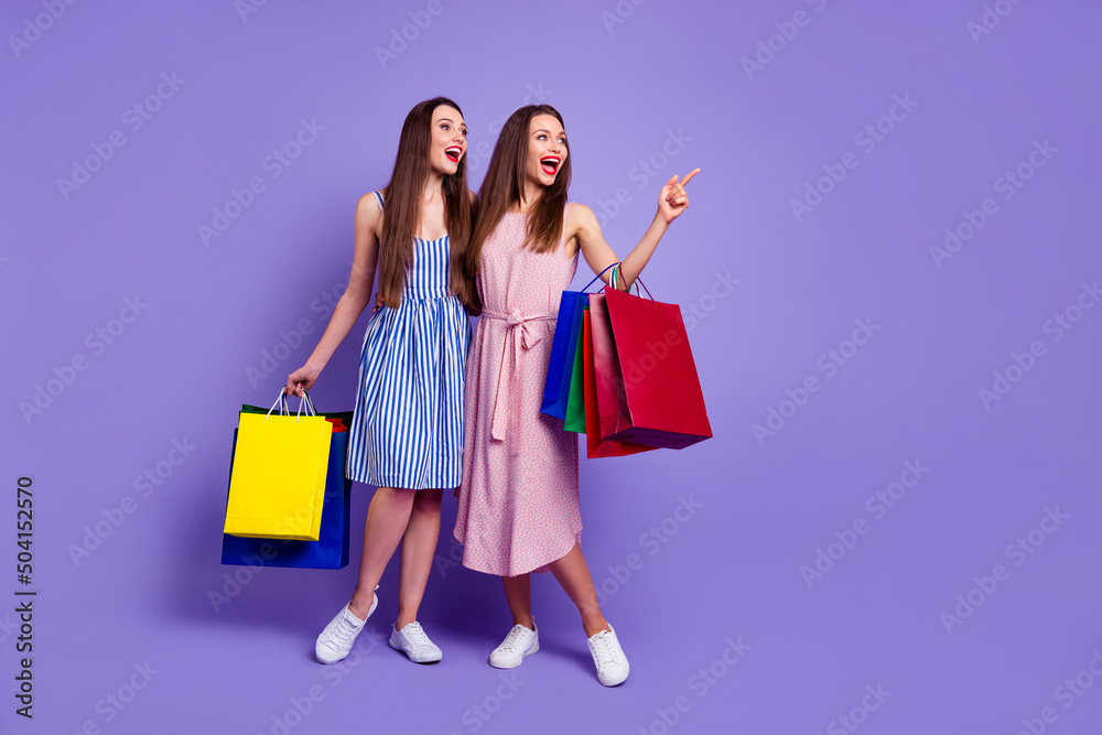 Photo of funky cute two best friends dressed summer clothes shopaholics pointing empty space isolated purple color background