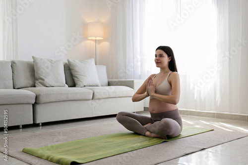 Young beautiful woman on second trimester of pregnancy doing yoga. Close up of pregnant female in sitting on a mat in lotus pose and meditating. Healthy pregnancy concept. Background, copy space.