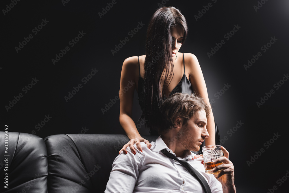 Sensual woman in dress touching boyfriend with glass of whiskey isolated on black. Sensual woman in dress touching boyfriend with glass of whiskey isolated on black.