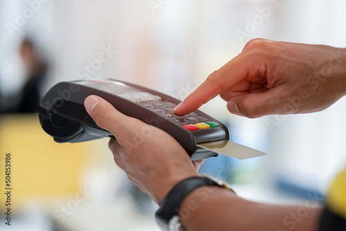 Cashier holding credit card reader machine on hand with insert card for payment process from customer, pressing the value number or price of products to charge the online payout, online deduction
