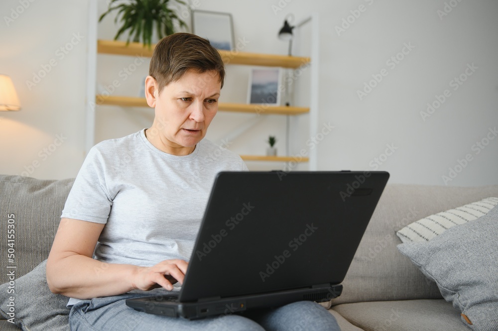 Technology, people and communication concept - Happy senior woman with tablet pc computer having video chat at home. Modern middle-aged 50s grandmother sit relax on couch in living room using laptop. Technology, people and communication concept - Happy senior woman with tablet pc computer having video chat at home. Modern middle-aged 50s grandmother sit relax on couch in living room using laptop.