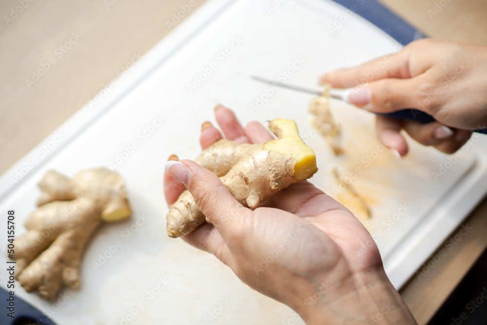 A woman peeling and cutting ginger to make a herbal drink.