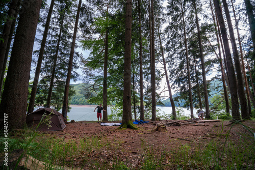 Two tents stands between trees in a pine forest on the river bank in the Carpathian mountains. Tourism and vacation concept. A mans sets up a tent. Arranges a camp.