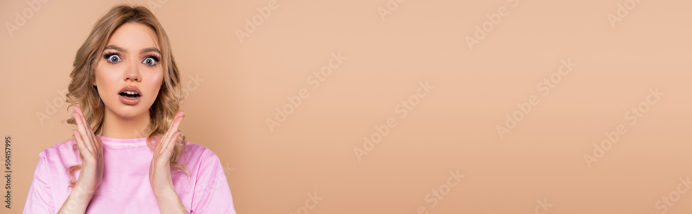 Fototapeta premium amazed woman looking at camera and showing wow gesture isolated on beige, banner.