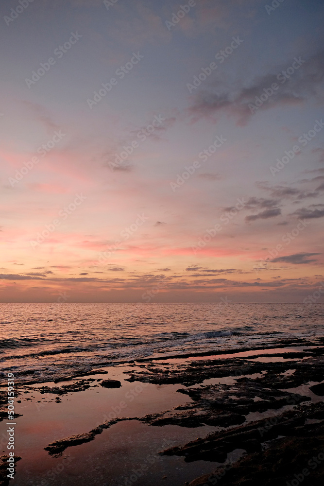 Beautiful seascape of sun setting over calm water with wind patterns and colorful pink spindrift clouds in the sky. Ocean view with horizon, background with a lot of copy space for text.