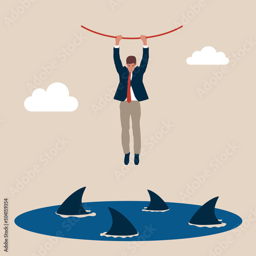 Businessman hangs on for dear life from a rope as he swings above a group of circling sharks in the sea. Risk taker, challenge to success, overcome difficulty or problem in crisis or entrepreneurship.