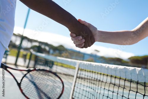Cropped hands of biracial female tennis players doing handshake over net at court on sunny day © wavebreak3