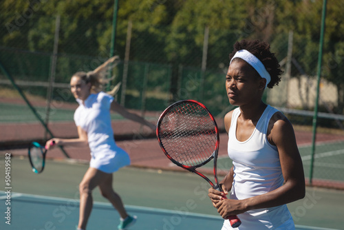 African american female tennis player playing with caucasian doubles partner at court on sunny day