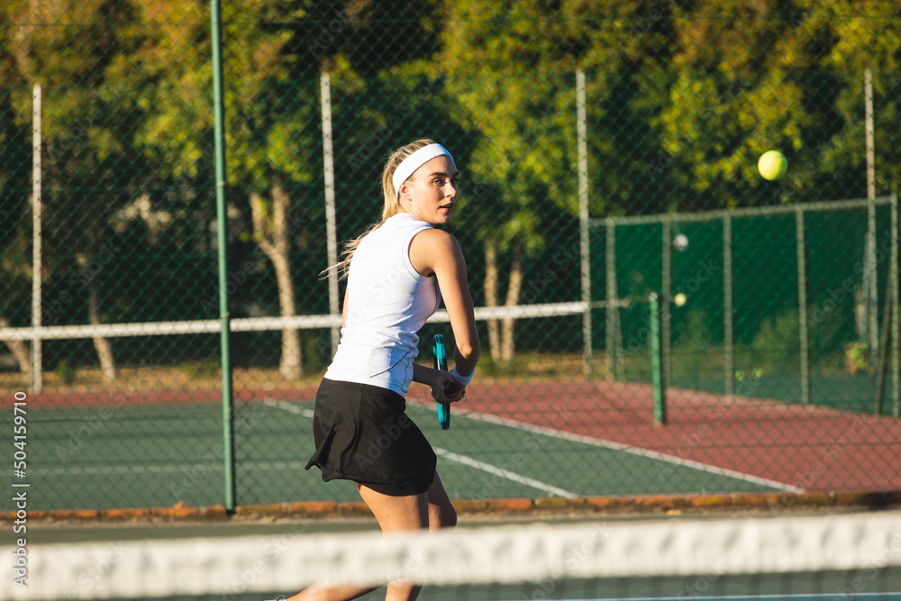 Beautiful young female caucasian tennis player hitting ball at court on sunny day Beautiful young female caucasian tennis player hitting ball at court on sunny day