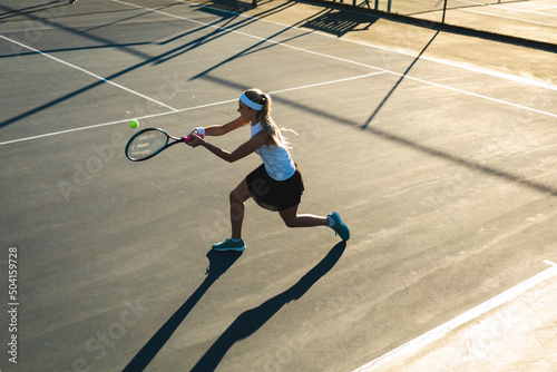 High angle view of young female caucasian tennis player hitting ball at court on sunny day