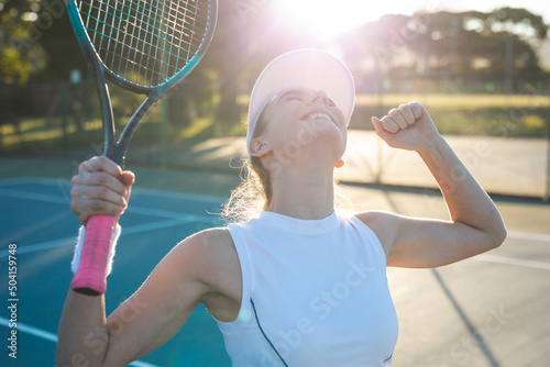 Excited young caucasian female tennis player celebrating game win at court while looking up